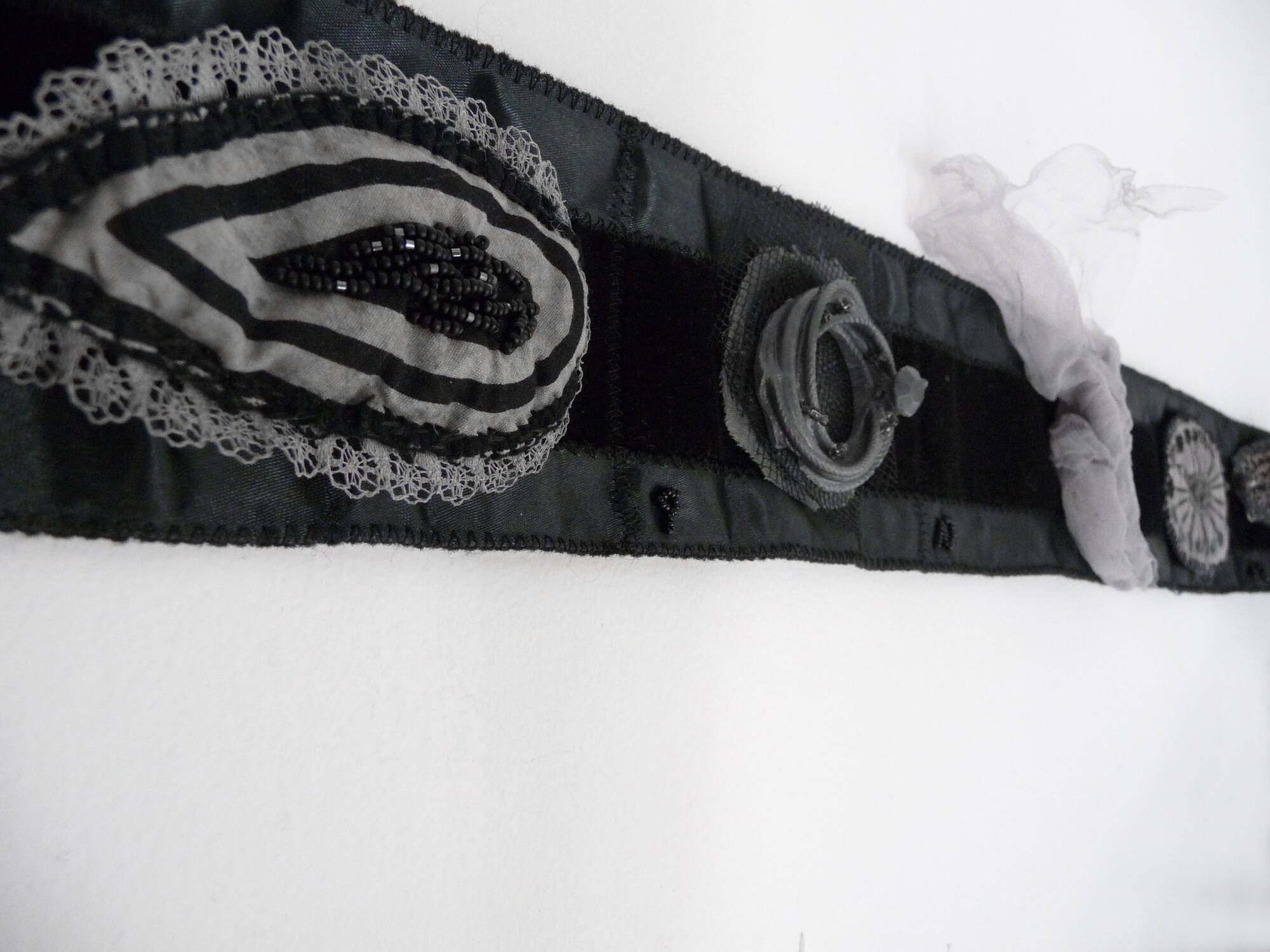 Closeup detail image of a strip of black fabric with textile brooches attached to it.